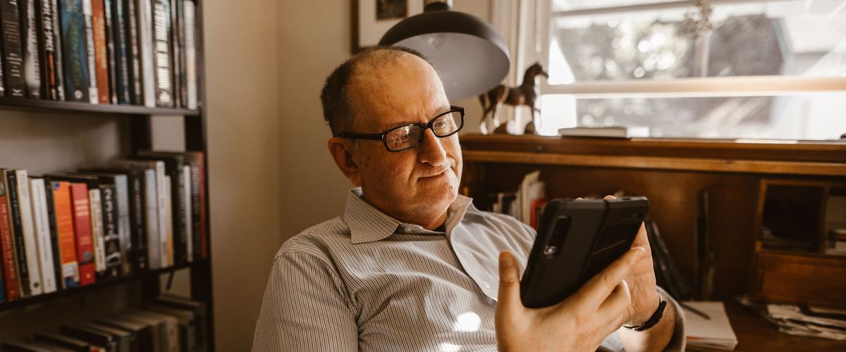 Starší muž s brýlemi si doma prohlíží chytrý telefon
