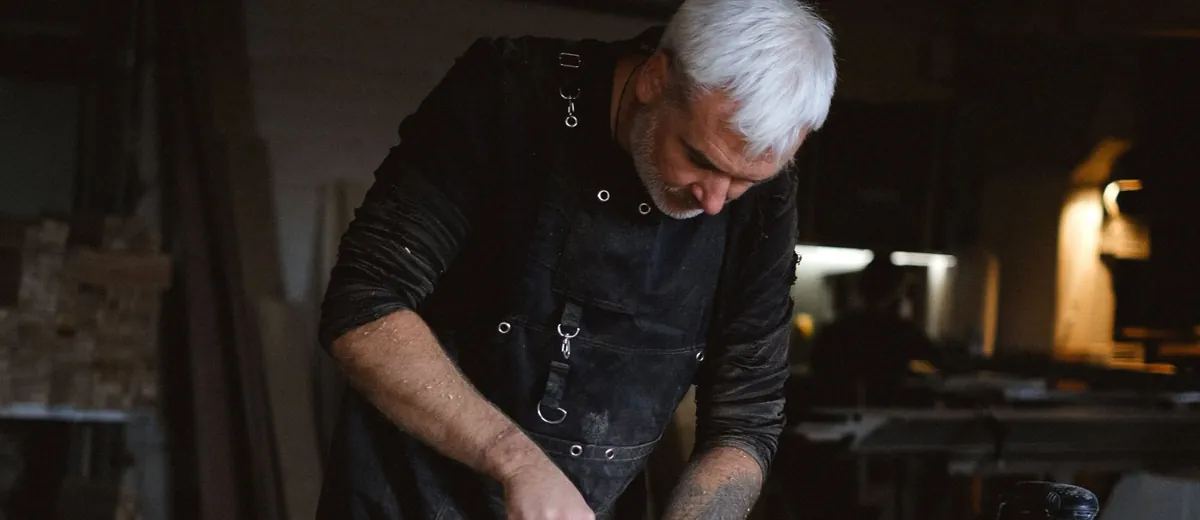 Šedovlasý truhlář pracuje v dílně s dlátem