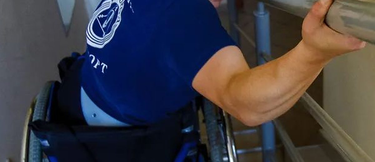Člověk na vozíku se drží zábradlí u schodiště